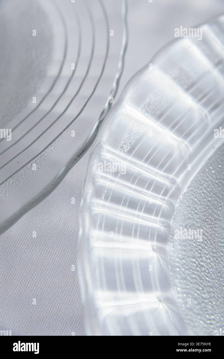 Detaillierte Nahaufnahme von Klarglasplatten mit Licht- und Schattenspiel auf strukturierter Oberfläche. Weiche, diffuse Beleuchtung hebt empfindliche Texturen hervor. Minimal, Stockfoto