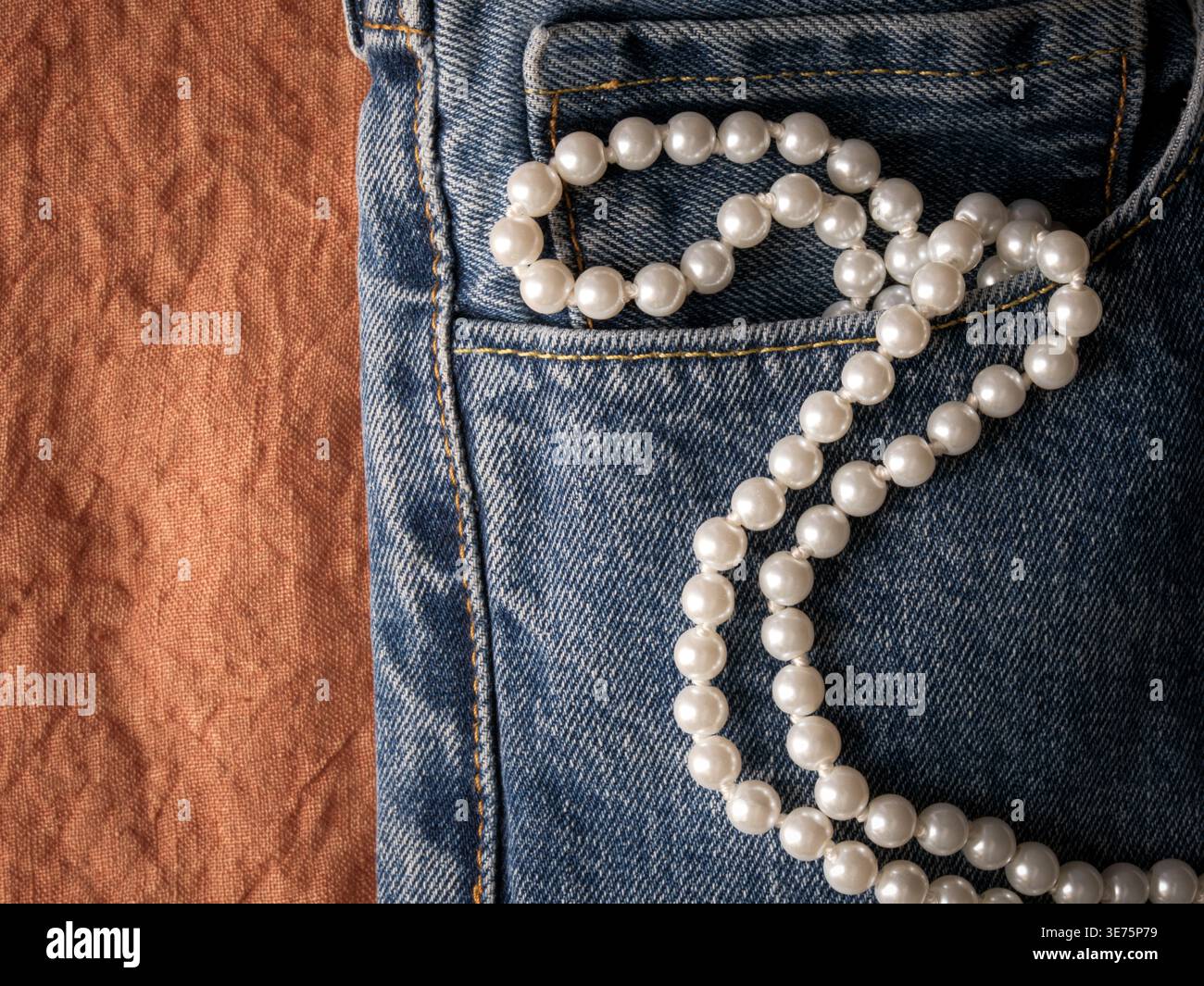 Perlenkette aus Denim-Tasche auf warmem rustikalem Leinenhintergrund, die ein feminines westliches Cowgirl-Modekonzept mit romantischem Vintage-Land schafft Stockfoto