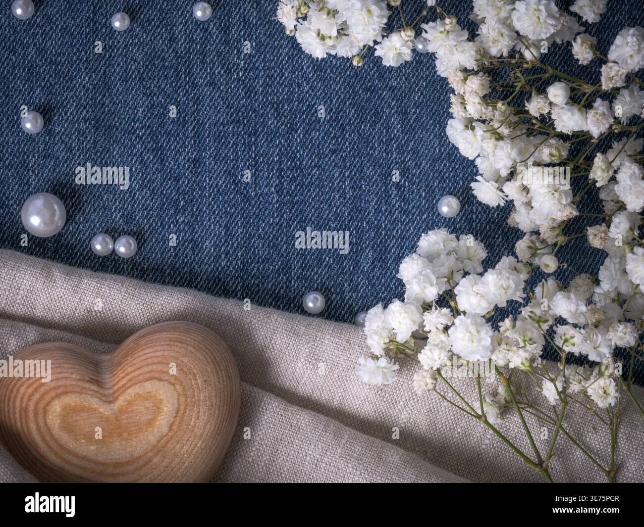 Hölzernes Herzsymbol, umgeben von Perlen und zarten weißen Blumen auf Denim-Stoff, schaffen rustikale westliche Romantik oder Landhochzeit Liebeskonzept. Stockfoto