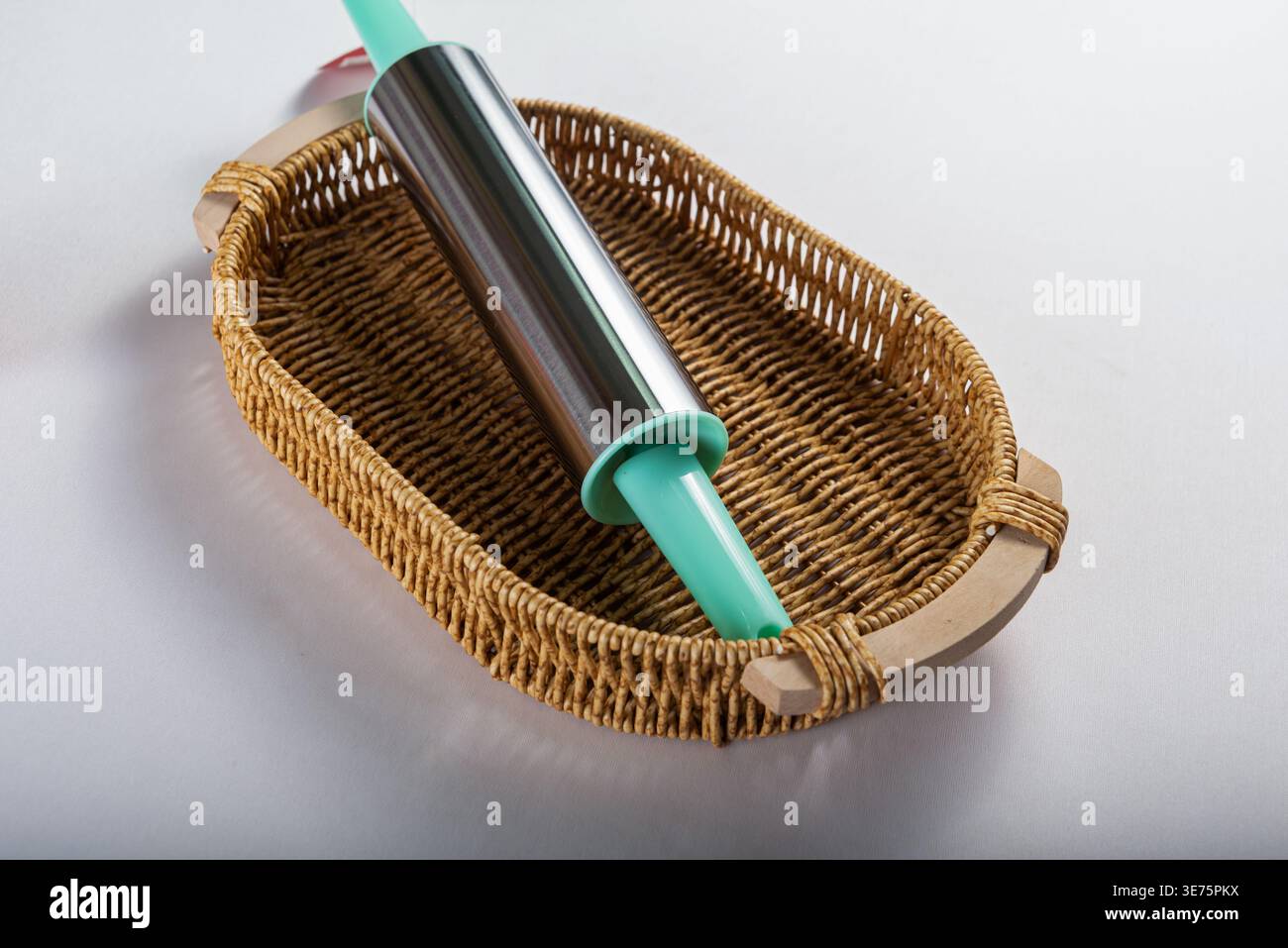 Rollstift mit blauen Griffen im Korb isoliert auf weiß. Die weiche Studiobeleuchtung sorgt für eine angenehme Textur. Neutrale Farbpalette. Backkonzept für f Stockfoto