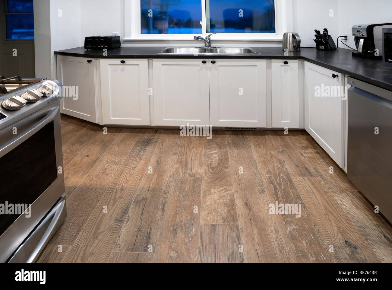 Moderne Küche mit Holzlaminatboden, Gasherd und Geschirrspüler und weißen Holzschränken Stockfoto