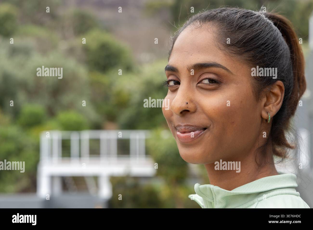 Indische Frau posiert an Deck, während sie lächelt, trägt einen mintgrünen Reißverschluss und zeigt einen Nasenbolzen Stockfoto