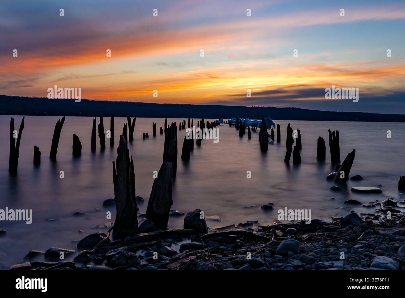 Dieses ruhige Landschaftsfoto fängt eine ruhige Küste bei Sonnenuntergang ein. Alte, verwitterte Holzpfähle ragen aus ruhigen Gewässern hervor. Stockfoto