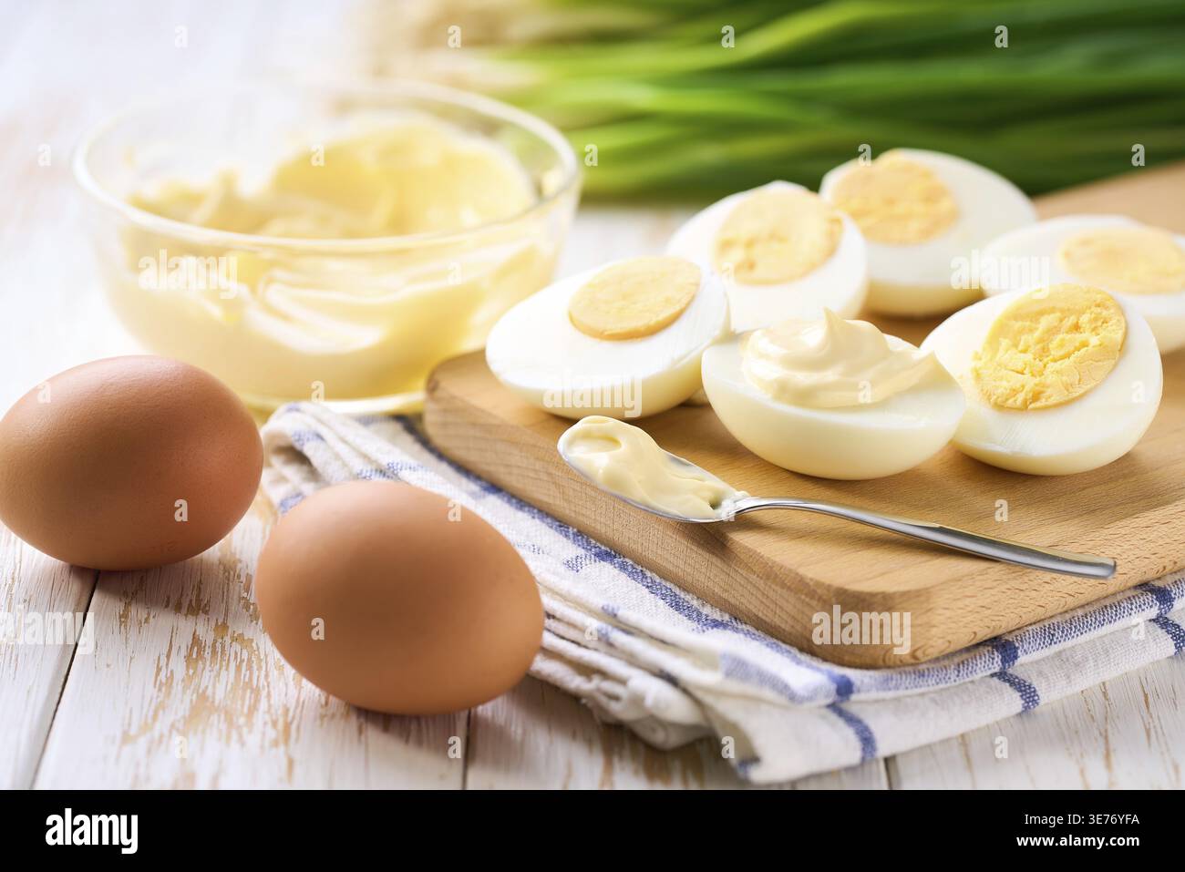Gesundes Frühstückskonzept, gekochte Hühnereier mit Mayonnaise und frisch geschnittenem Schnittlauch auf einem Holztisch Stockfoto