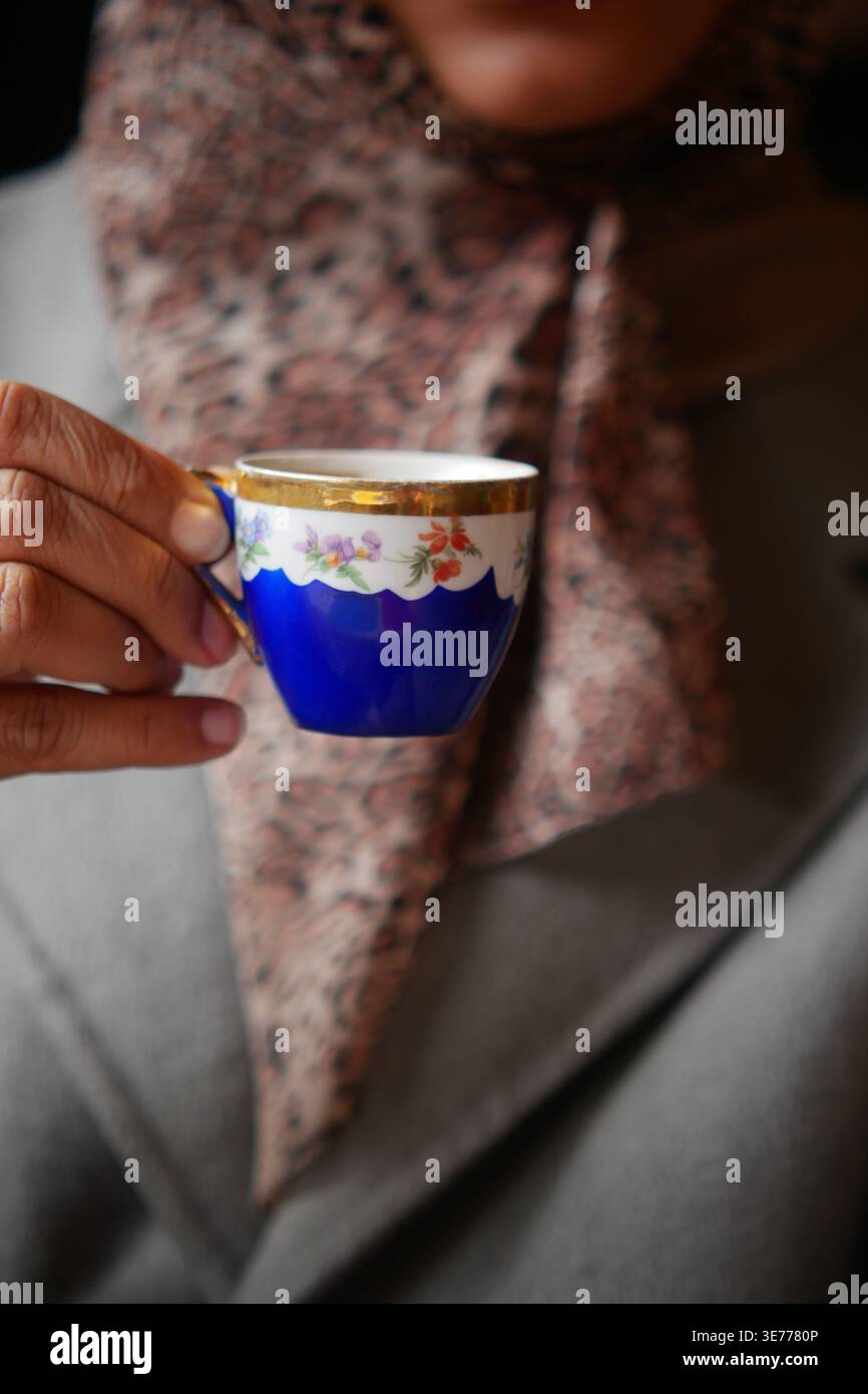 Tasse, die von einer Person gehalten wird, die einen Schal trägt, während eines sozialen Moments Stockfoto