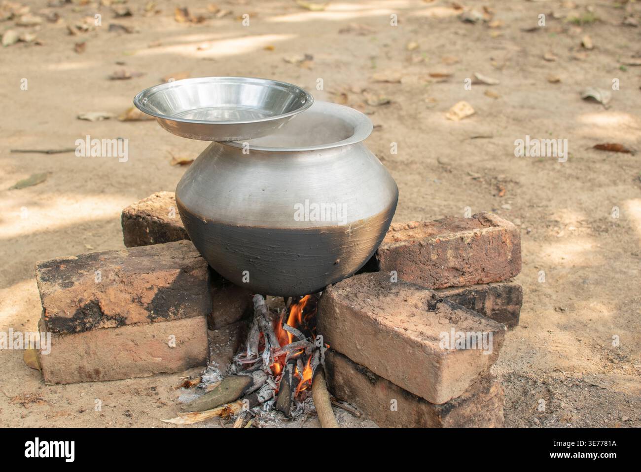 Ein mit Ton beschichteter Aluminiumtopf kocht draußen über einem Holzfeuer und unterstreicht traditionelle Methoden für gleichmäßige Hitze und Geschmack. Stockfoto