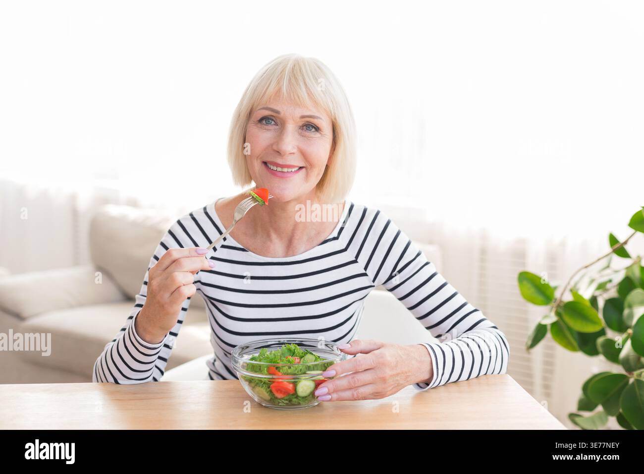 Glückliche Seniorin isst zu Hause frischen Salat Stockfoto