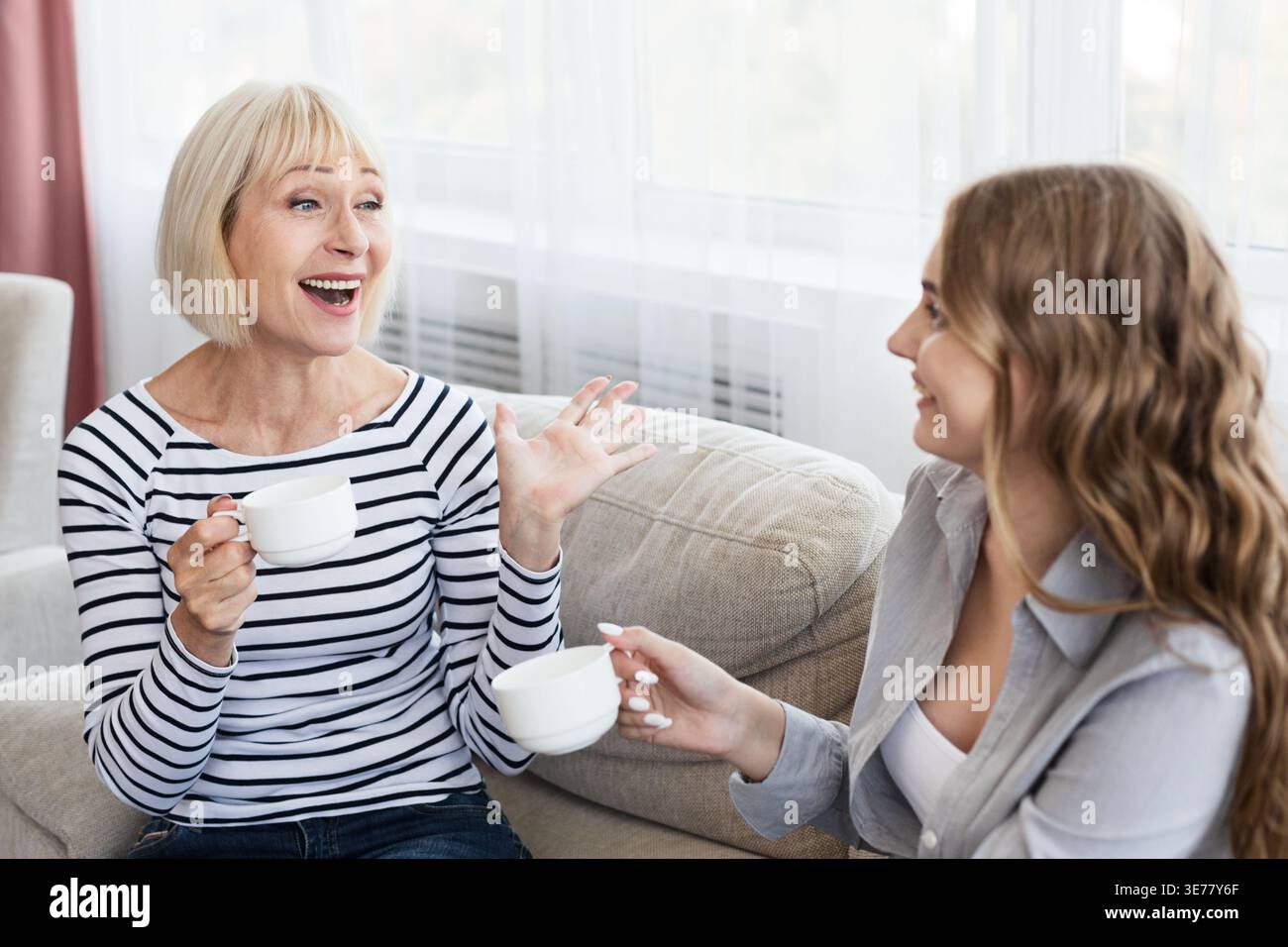 Glückliche, reife Mutter und Tochter trinken Kaffee und reden Stockfoto