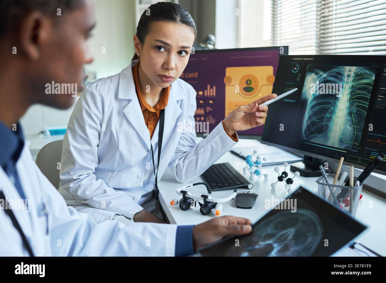 Porträt einer asiatischen Ärztin, die mit einem schwarzen Kollegen über Lungenscan spricht und diagnostische Bildgebung auf Monitoren überprüft. Ideal für Teamarbeit im Gesundheitswesen, Radiologie und Diagnosemarketing Stockfoto