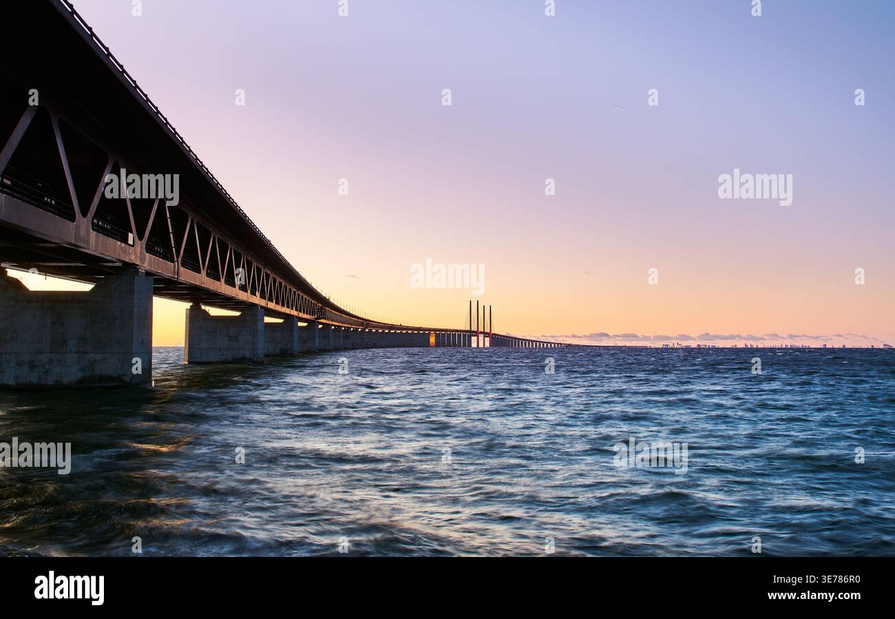 Sonnenuntergang über der Öresund-Brücke, die Malmö, Schweden, mit Kopenhagen, Dänemark verbindet, bis in die Ferne über dem plätschernden Meer mit einem warmen Himmel Stockfoto