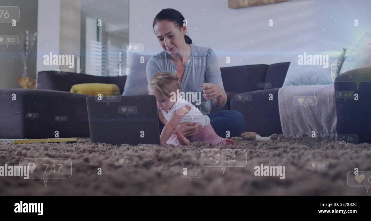 Sitzende Mutter in hellblauem Oberteil, die das Baby auf dem Teppich hält, und den Laptop mit überlagerten sozialen Kennzahlen ansieht Stockfoto