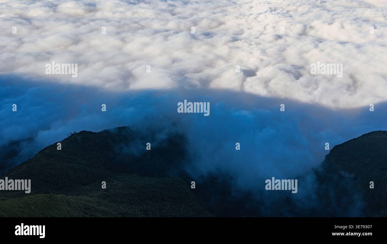 Die Wolkendecke aus der Luft taucht wie ein langsamer Wasserfall über bewaldete Bergrücken auf Madeira und trifft auf kühle Schatten und verschleiernde Gipfel in der Nähe von Pico do Arieiro und Pico Ru Stockfoto