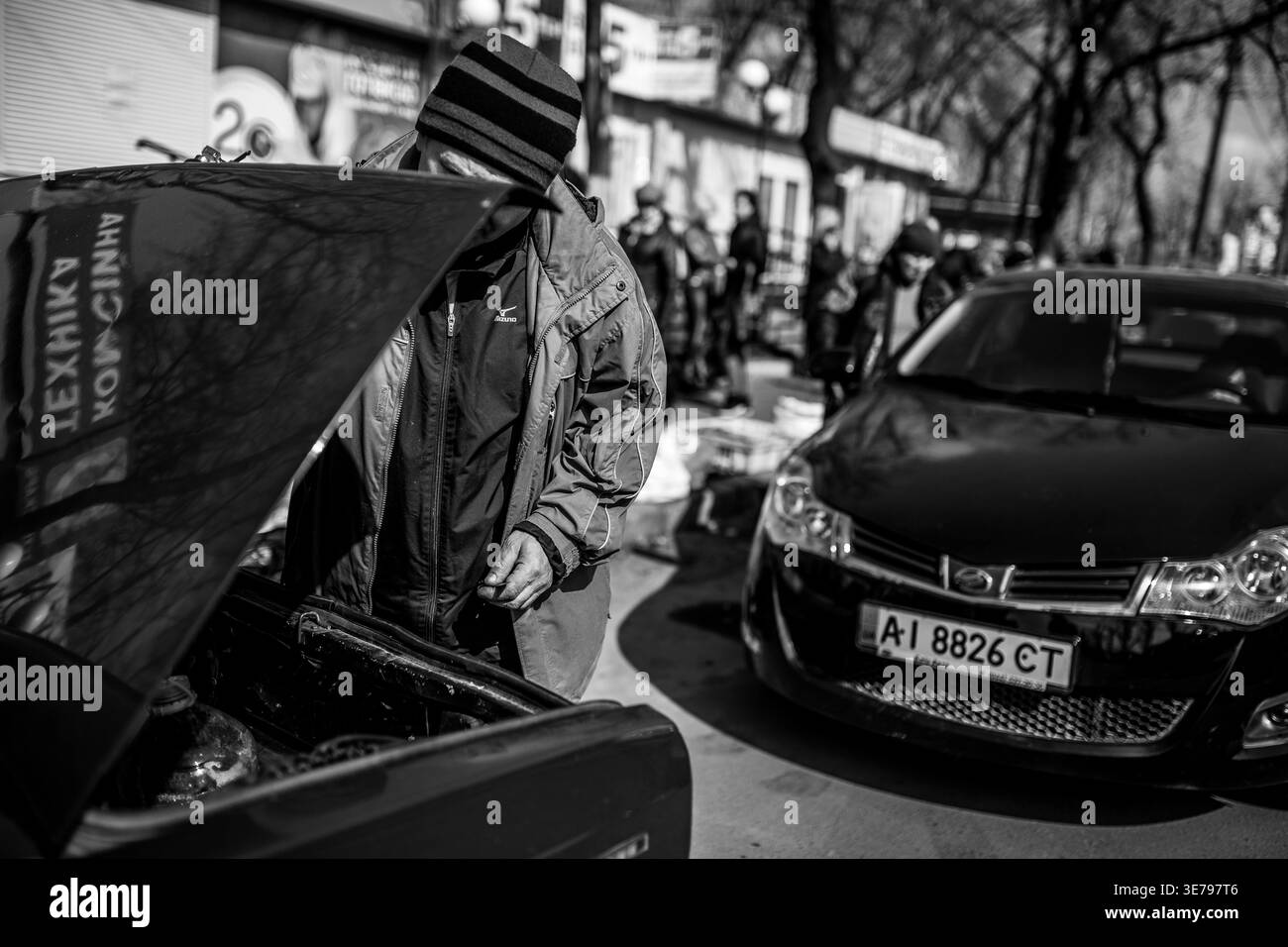 Darnytsia, Kiew, Ukraine – 21. März 2014: Ein einfarbiger Außenbereich schoss eine Person in einer gestreiften Mütze und Jacke, die mit mir den Motor eines schwarzen Autos inspizierte Stockfoto