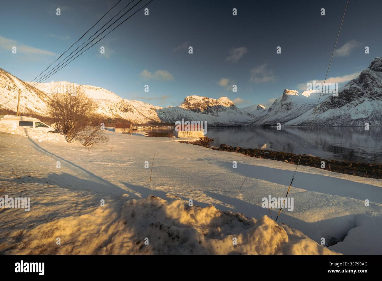 Blick auf eine ruhige Winterlandschaft, wo der schneebedeckte Boden auf das stille Wasser trifft und die majestätischen, schneebedeckten Berge Indregård, TROM reflektiert Stockfoto