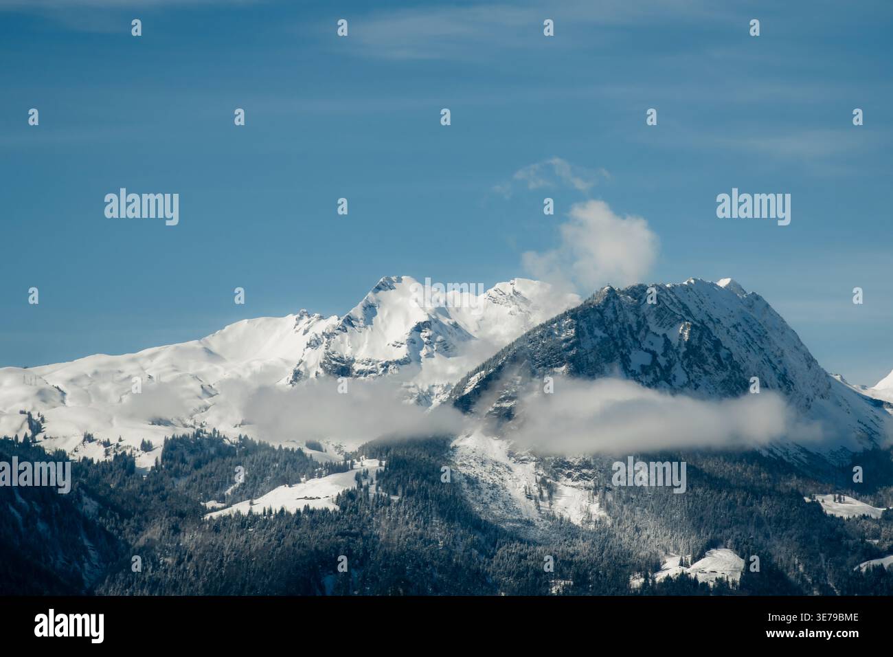 Blick auf schneebedeckte Gipfel durchdringen den azurblauen Himmel, ihre majestätischen Formen werden von ätherischen Wolken weich, eine Wintergeschichte entfaltet sich, Train from Luzern Stockfoto
