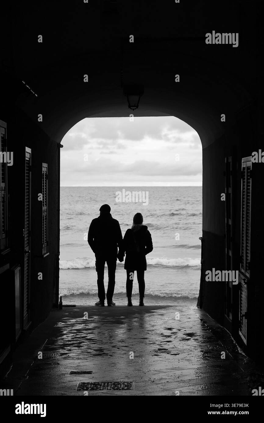 Ein Paar hält die Hände, während er das Meer von ​​Alassio unter einem Bogen bewundert Stockfoto