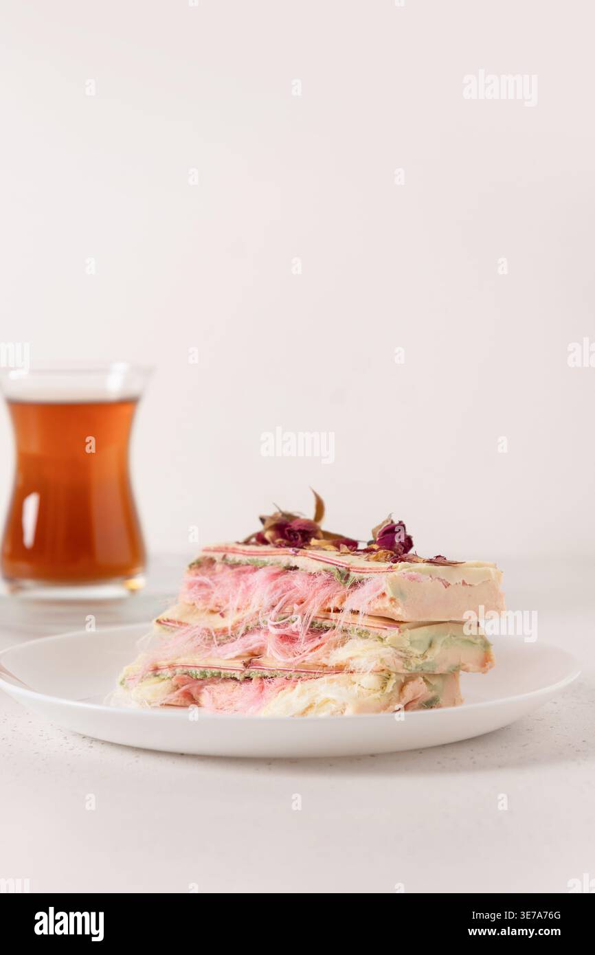 Ungewöhnliches Dessert mit Zuckerwatte, verziert mit getrockneten Rosen auf weißem Teller und Tee, minimalistisches Essenskonzept für Café-Menü, kreatives Gas Stockfoto