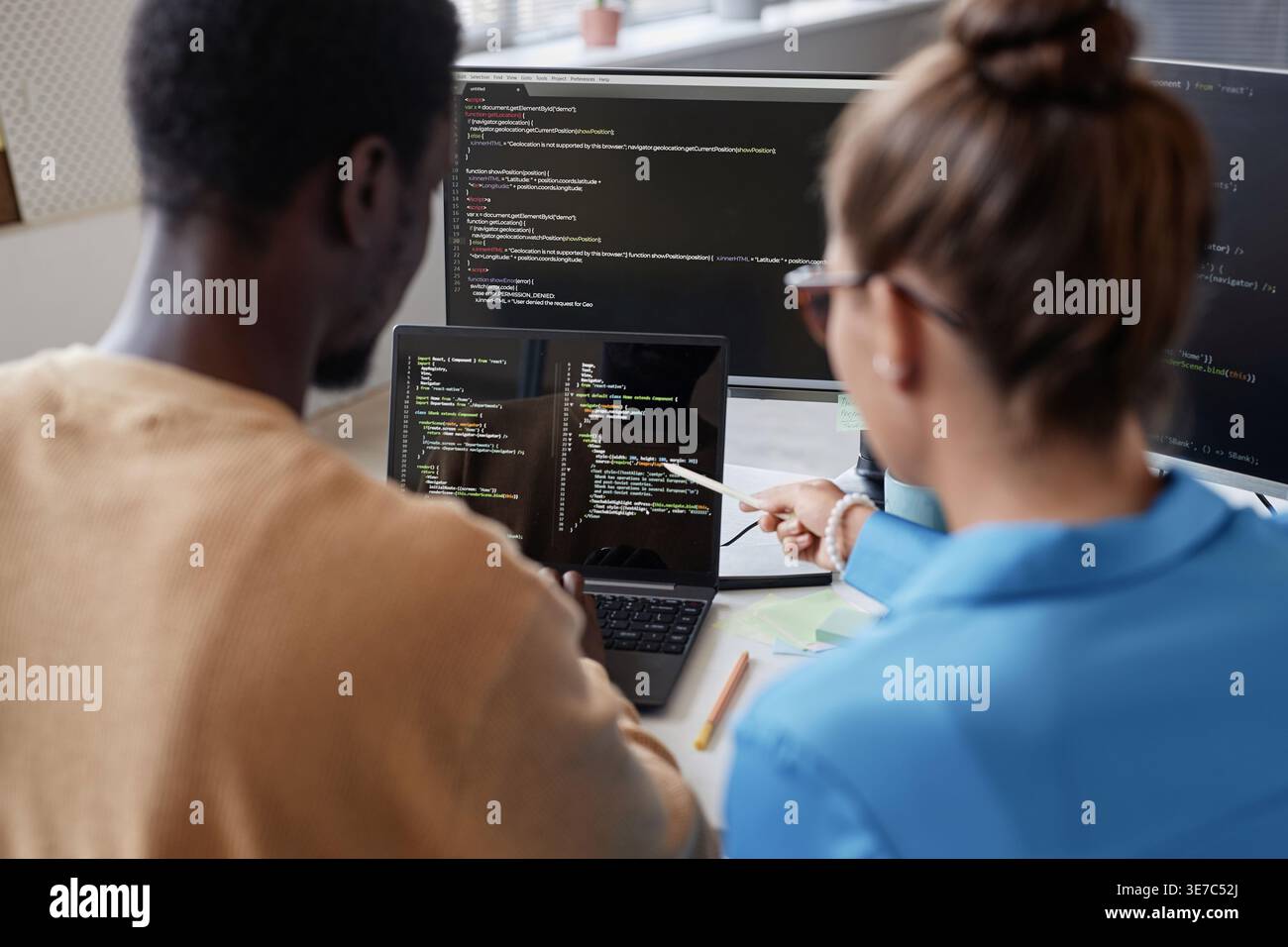 Schwarze männliche und kaukasische Programmiererinnen diskutieren Computercodes auf Laptop, sitzen zusammen am Tisch im Büro Stockfoto