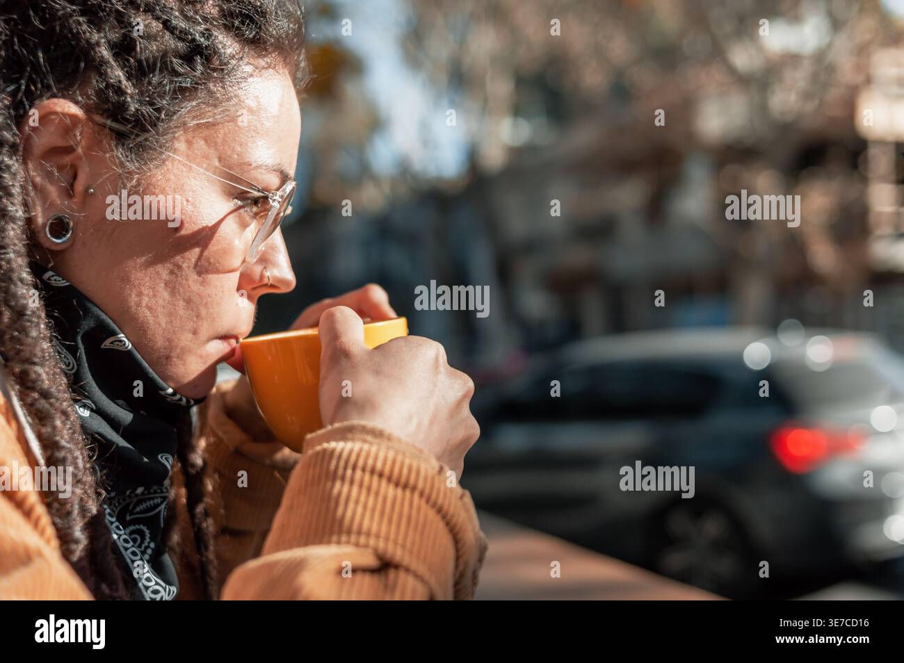 Hispanische Frau mit Dreadlocks, die eine Brille trägt und tagsüber Kaffee trinkt, während sie am Tisch im Café im Freien sitzt Stockfoto