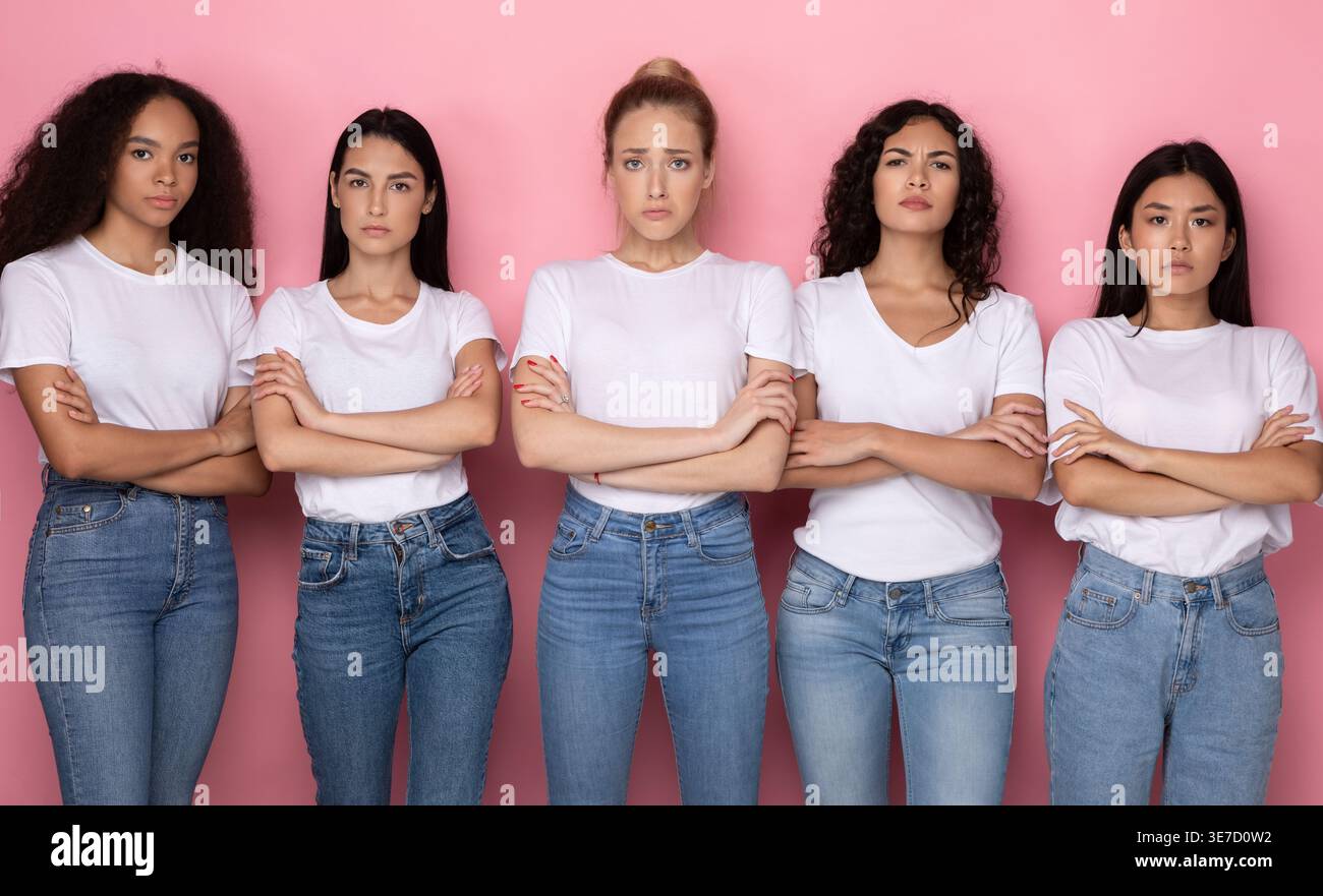 Eine Gruppe von Frauen mit weißen Hemden und Jeans, die mit überkreuzten Armen vor rosa Hintergrund im Studio stehen Stockfoto
