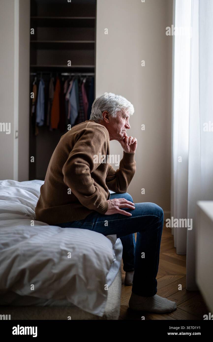 Seniorenmann allein zu Hause mit Hand über Mund, die in Angst und Apathie reflektiert. Demenzkrankheiten Stockfoto