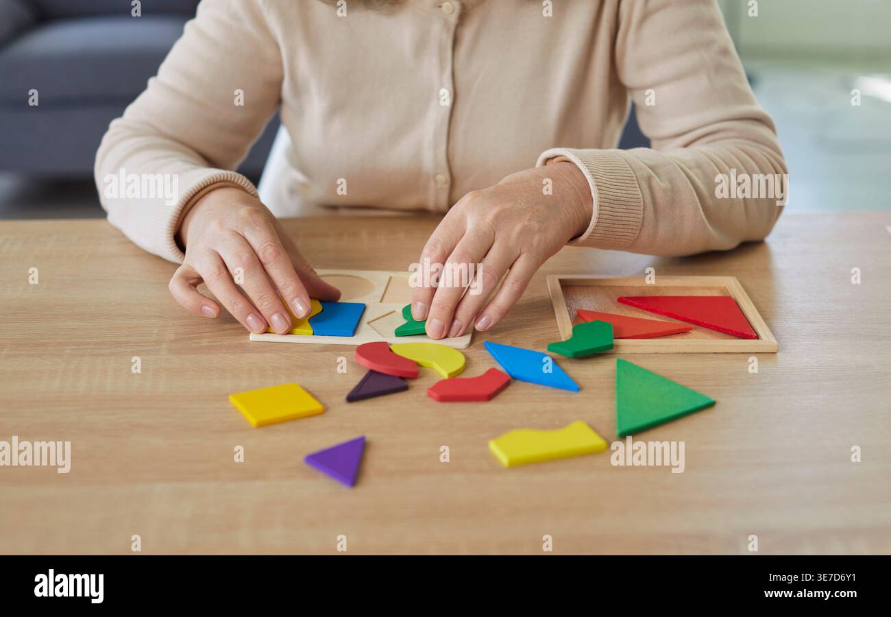 Abgeschnittenes Porträt einer älteren Frau, die zu Hause geometrische Holzfiguren sammelt und am Tisch sitzt Stockfoto