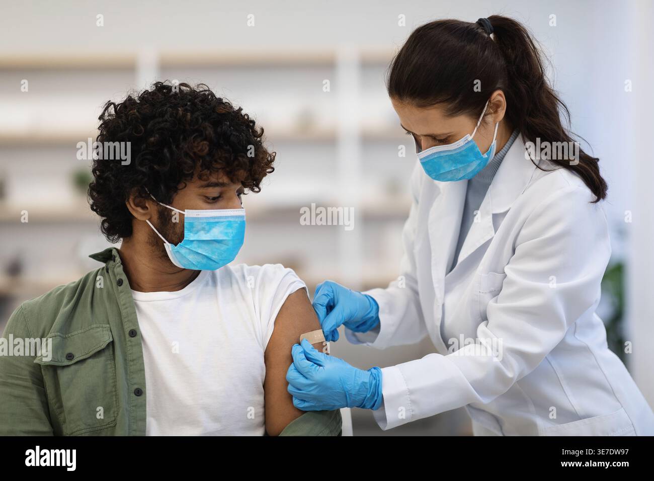 Asiatische Ärztin in Operationshandschuhen, die Klebeband an der Schulter eines asiatischen männlichen Patienten auf Stuhl in der Klinik anbringen Stockfoto
