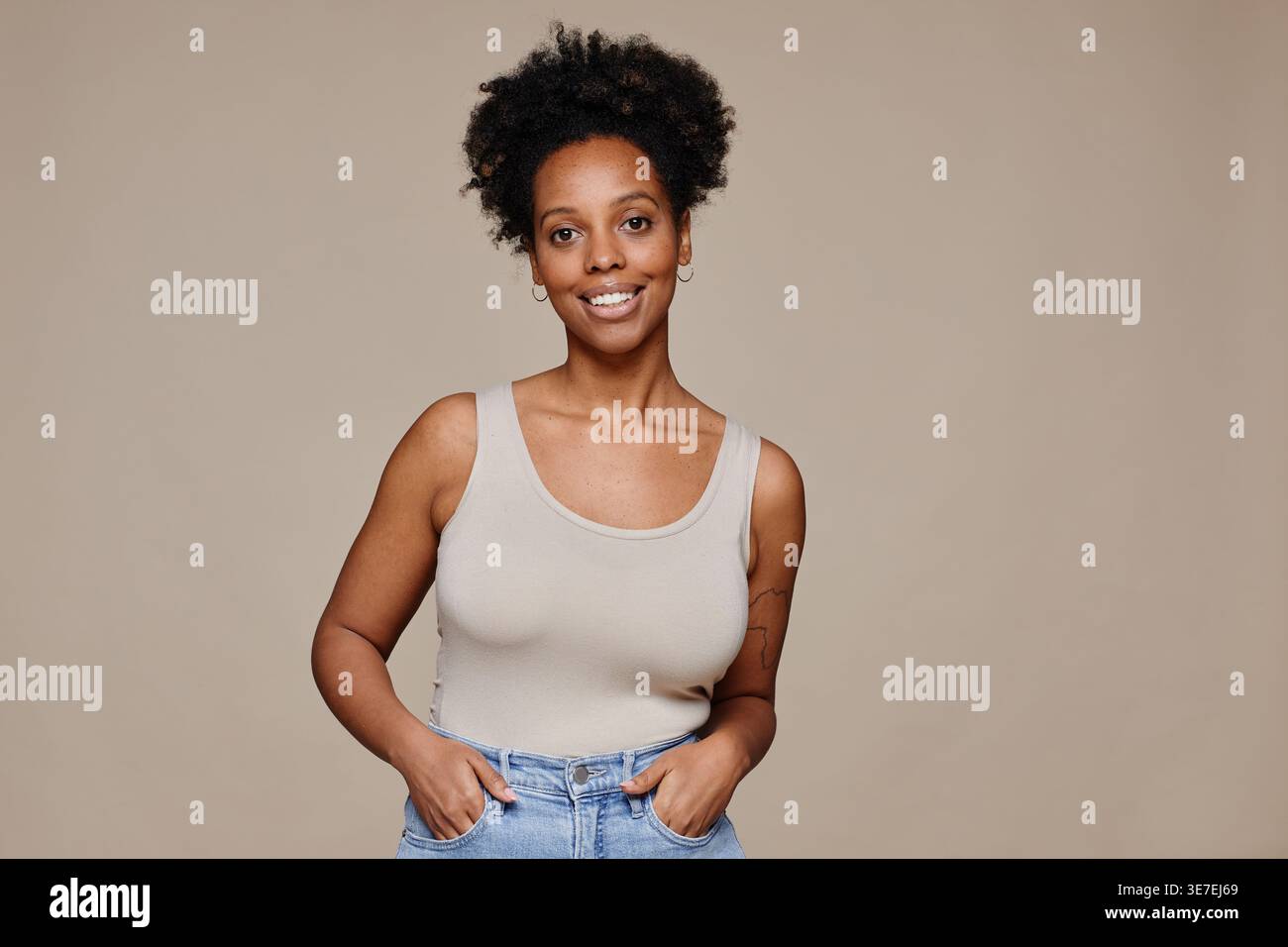 Porträt einer jungen afroamerikanischen Frau, die vor neutralem Hintergrund und natürlicher Schönheit lächelt und dabei die Kamera anschaut Stockfoto