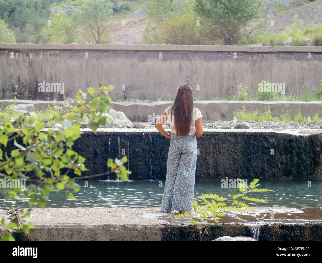 Gemischte Rassenfrau mit Hand auf Taille, die tagsüber auf Beton in der Nähe des Flusses steht Stockfoto