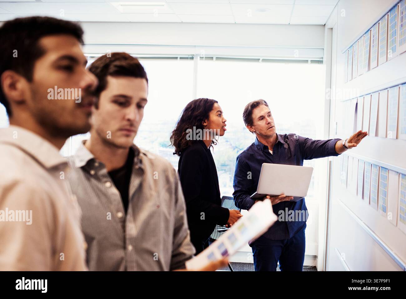 Schwarze Frau im Business-Anzug analysiert chLifestyles an der Wand mit einem kaukasischen Kollegen im Büro Stockfoto