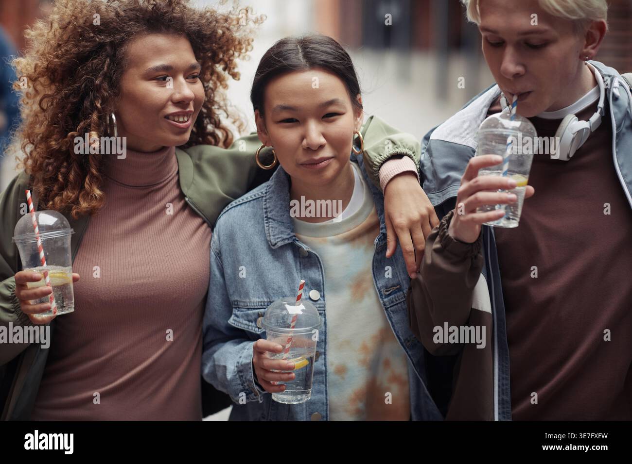 Verschiedene Freunde halten Limonade und spazieren durch die Straßen Stockfoto