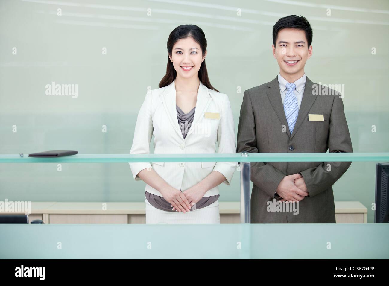 Lächelnde chinesische männliche und weibliche Rezeptionistin stehen an der Rezeption im Hotel Stockfoto