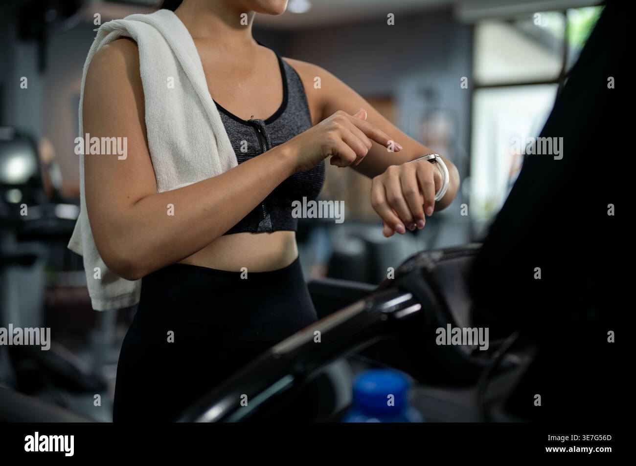 Thailändische Frau in Fitnesskleidung, die ihre Smartwatch beim Gehen auf dem Laufband im Fitnessstudio festlegt Stockfoto