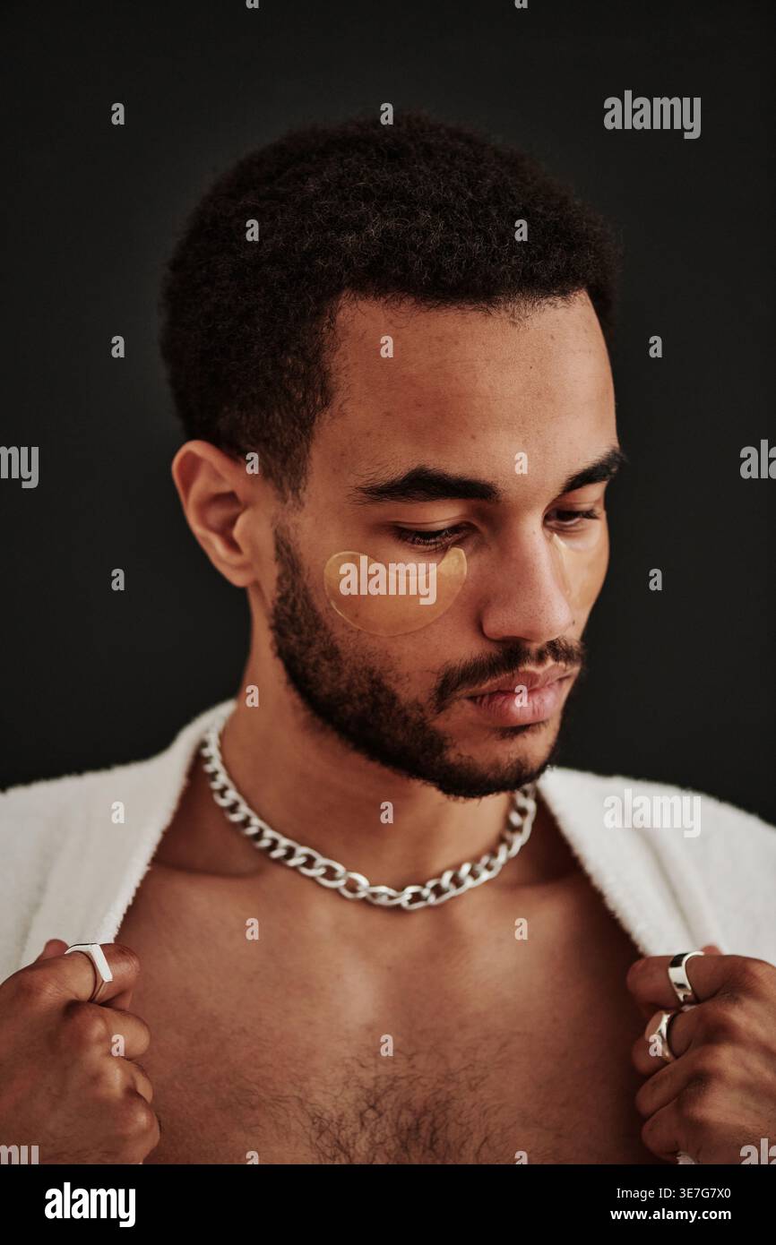 Ernsthafter gemischter bärtiger Mann mit Augenflecken, die das Hemd vor schwarzem Hintergrund im Studio befestigen Stockfoto