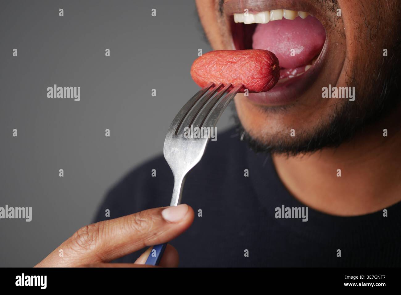 Nahaufnahme Mann Isst Wurst Auf Der Gabel, Zeigt Mund, Zunge Und Hand Stockfoto