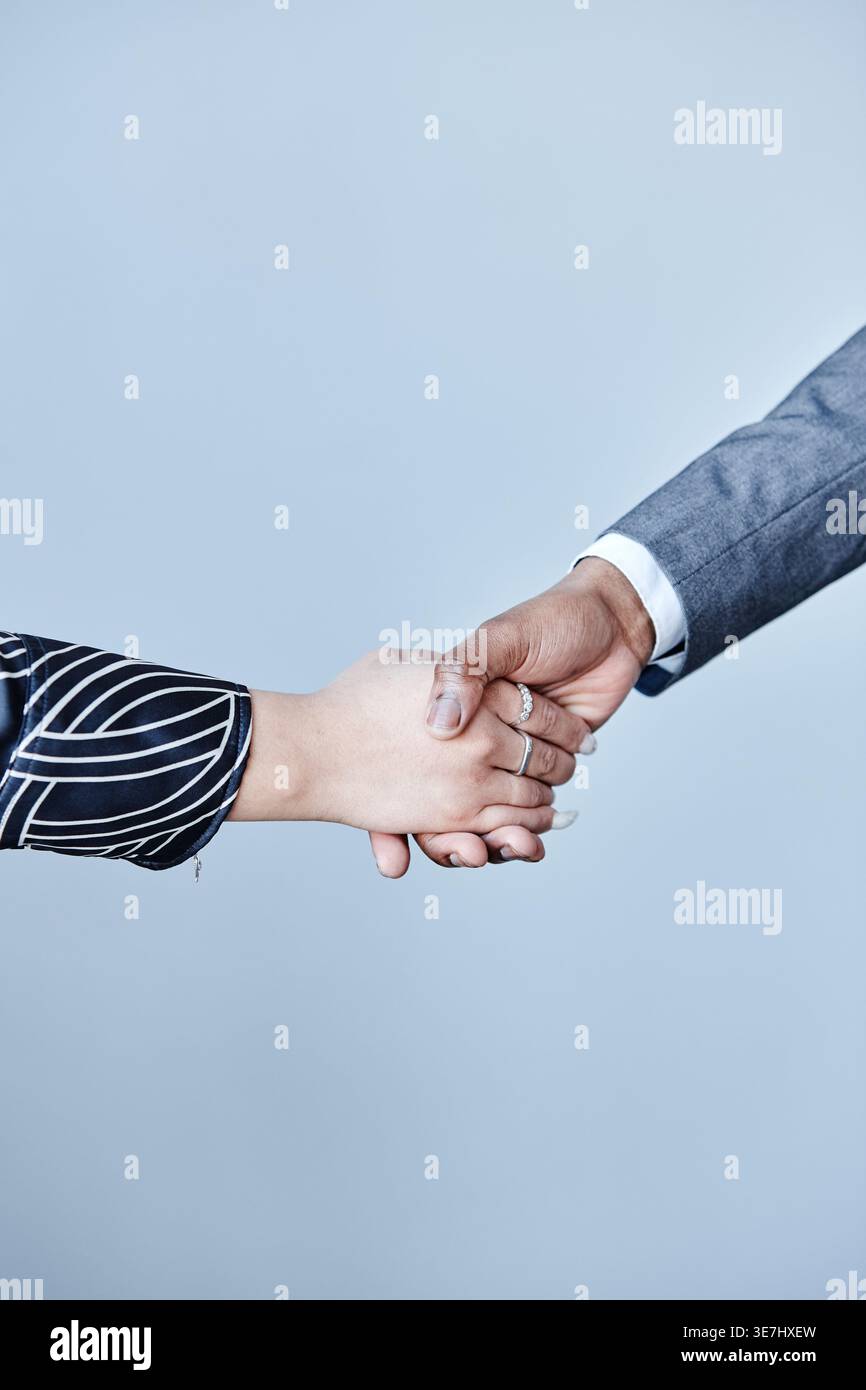 Hände eines schwarzen Geschäftsmannes und einer Frau, die Hände schütteln, die im Büro vor grauem Hintergrund stehen Stockfoto