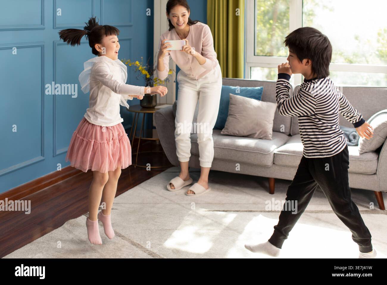 Chinesische Mutter, die ein Video ihrer Kinder macht, die an sonnigen Tagen zu Hause tanzen Stockfoto