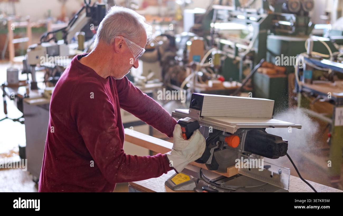 Erfahrener Holzarbeiter, der Holz mit Gehrungssäge in der Werkstatt sägt Stockfoto