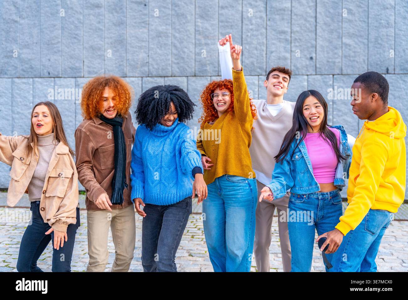 Fröhliche, abwechslungsreiche Gruppe von Freunden, die tagsüber Spaß beim Tanzen in der Nähe der grauen Wand auf der Straße haben Stockfoto