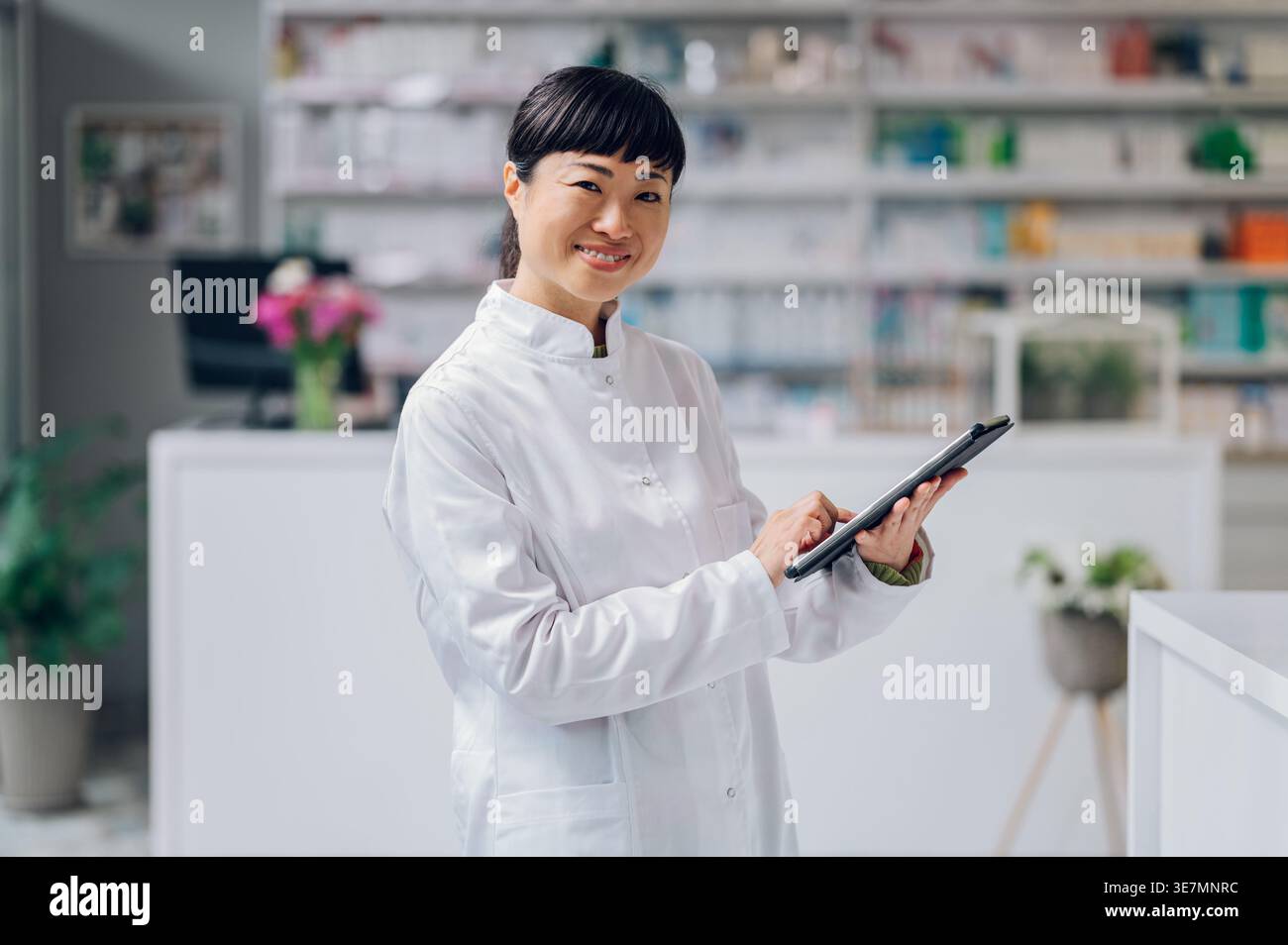 Japanische Apothekerin mit Tablette, die in der Apotheke gegen den Zähler steht Stockfoto