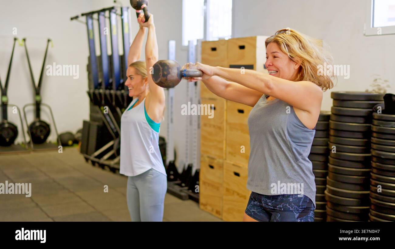 Frauen, die mit Kettlebells trainieren und Kraftübungen im Fitnessstudio durchführen Stockfoto