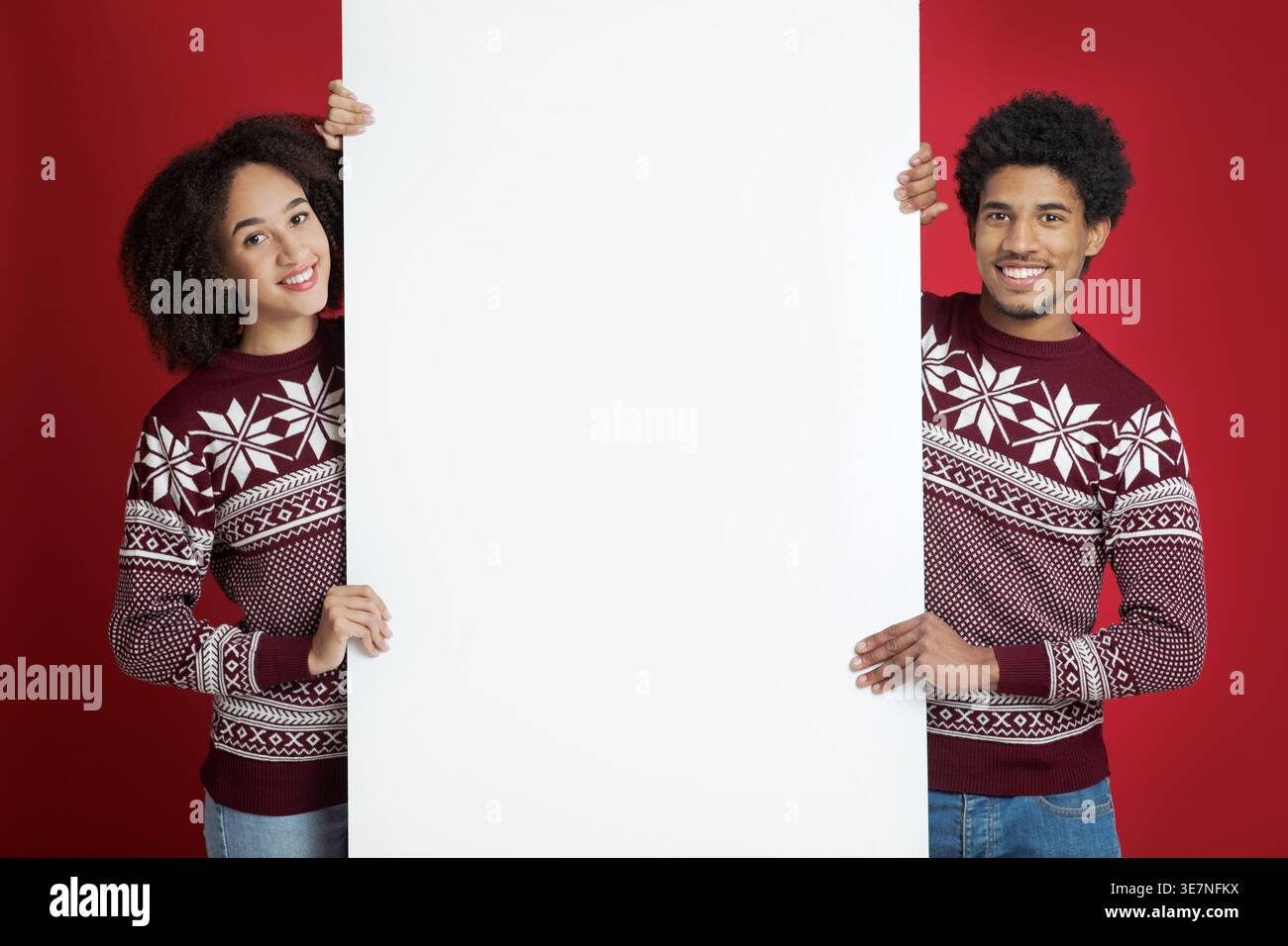 Schwarzes Paar in rotem Pullover, das weißes Banner vor rotem Hintergrund im Studio zusammenhält Stockfoto