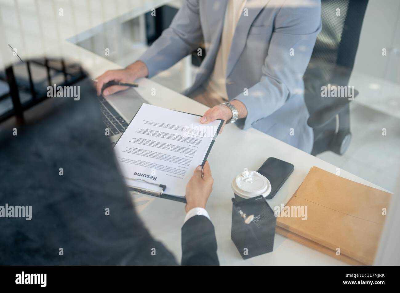 Zugeschnittenes Bild eines asiatischen Geschäftsmannes, der am Laptop arbeitet und Dokumente zu einer Kollegin bringt, während er am Tisch im Büro sitzt Stockfoto
