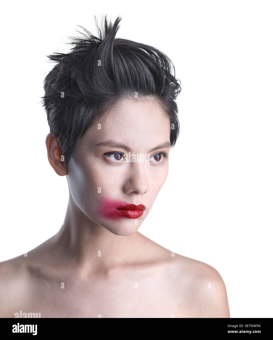 Asiatische Frau mit unordentlichem rotem Lippenstift und zerzausten, stacheligen Haaren, die vor weißem Hintergrund im Studio wegschauen Stockfoto