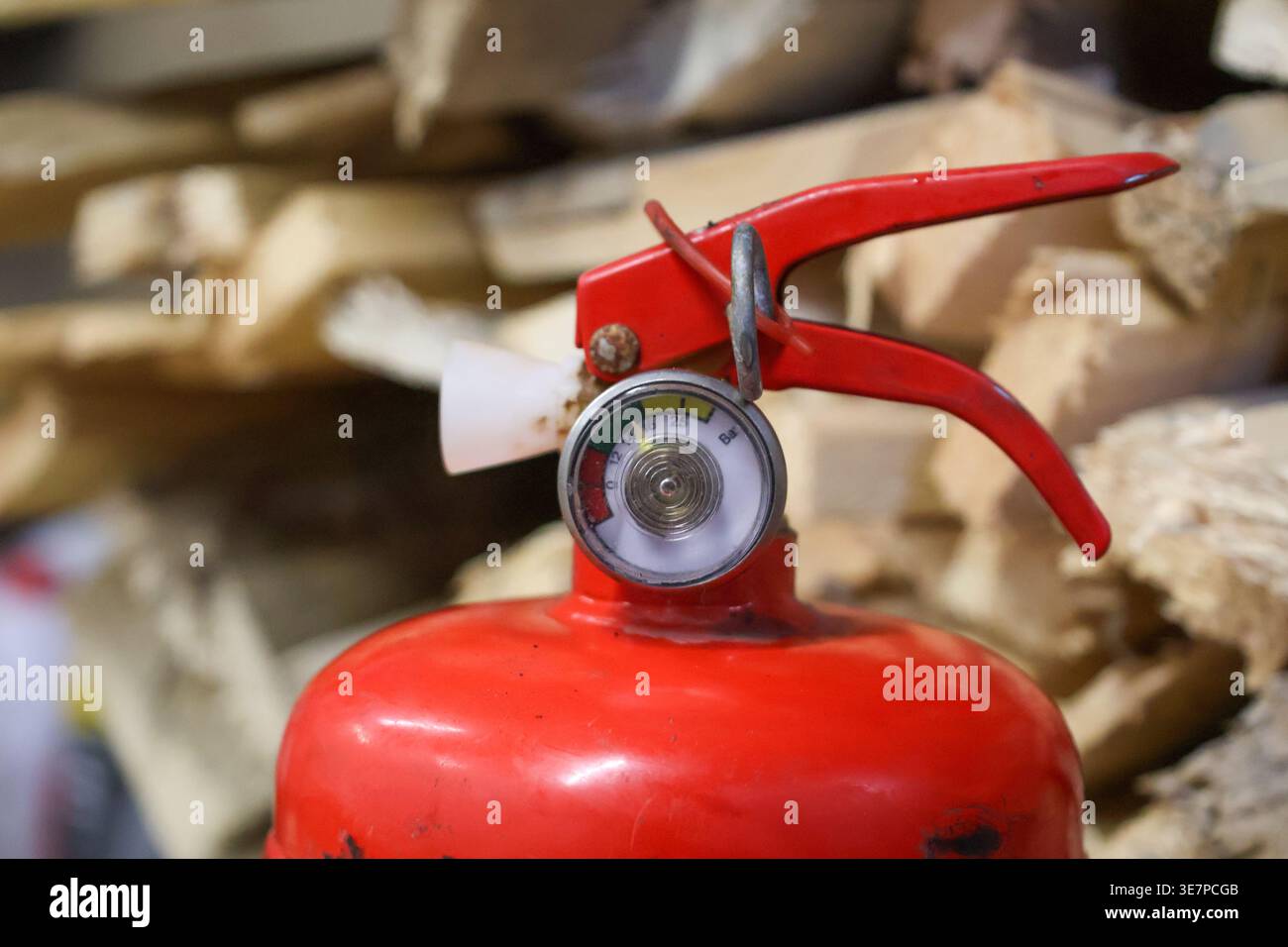 Ein Feuerlöscher wird in Nahansicht mit Anzeige und Auslöser angezeigt. Es befindet sich in der Nähe von Holzstapeln in einem Lagerbereich. Stockfoto