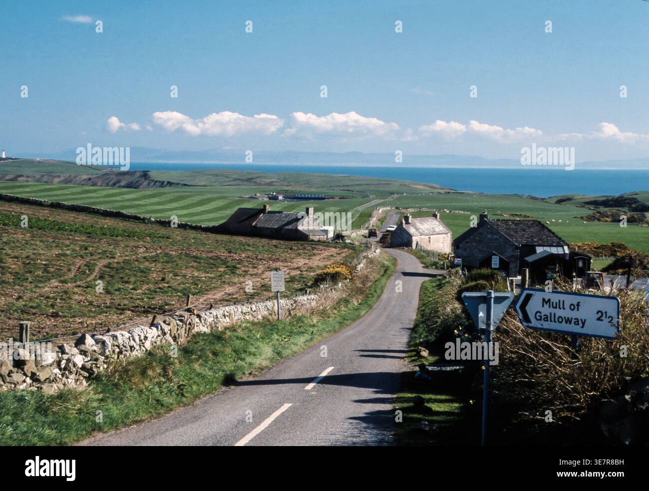 Die malerische Landstraße schlängelt sich in Richtung Mull of Galloway, gesäumt von Steinhäusern und Meerblick. Stockfoto