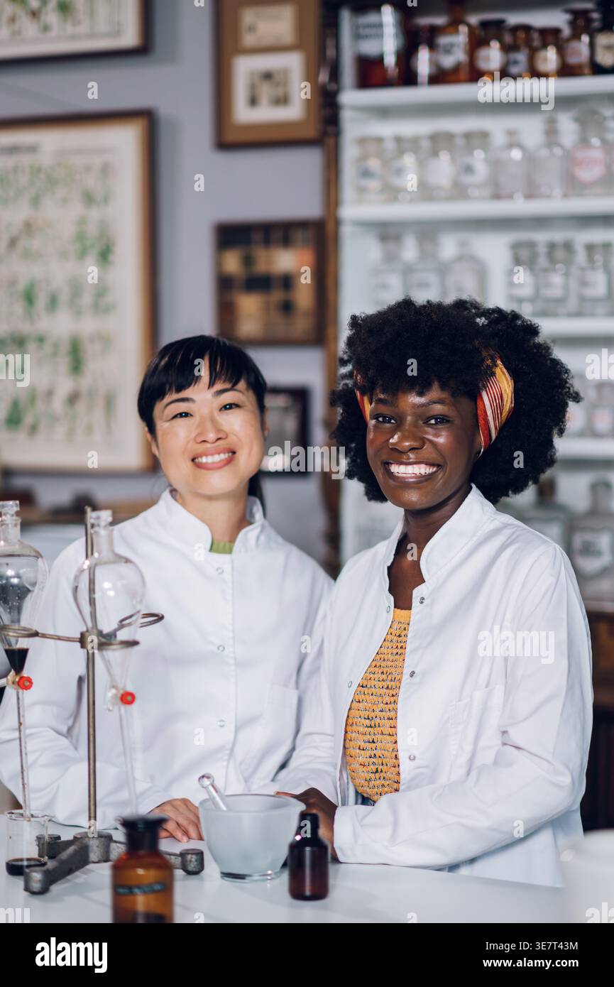 Japanische und schwarze Apothekerinnen stehen zusammen an der Theke in einer Vintage-Apotheke Stockfoto