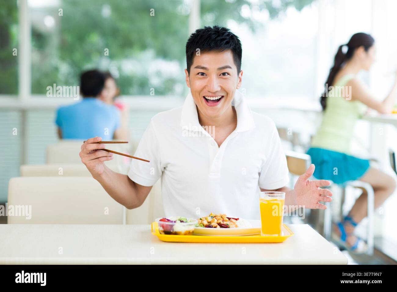 Fröhlicher Chinese, der Essstäbchen beim Essen benutzt, während er am Tisch im Restaurant sitzt Stockfoto