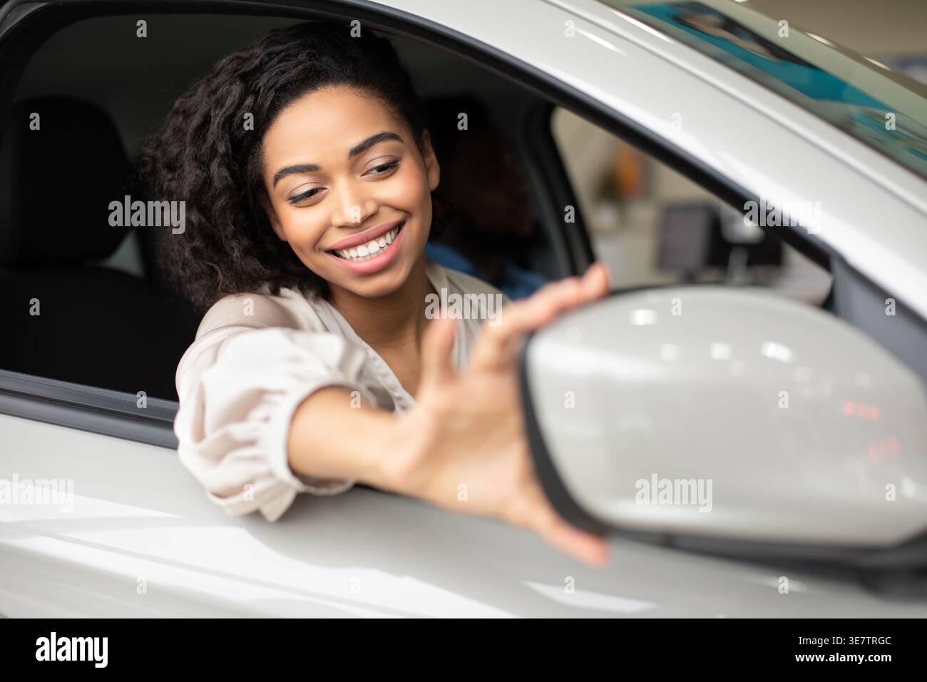 Schwarze Frau, die den Seitenspiegel verstellt, während sie auf dem Beifahrersitz sitzt Stockfoto