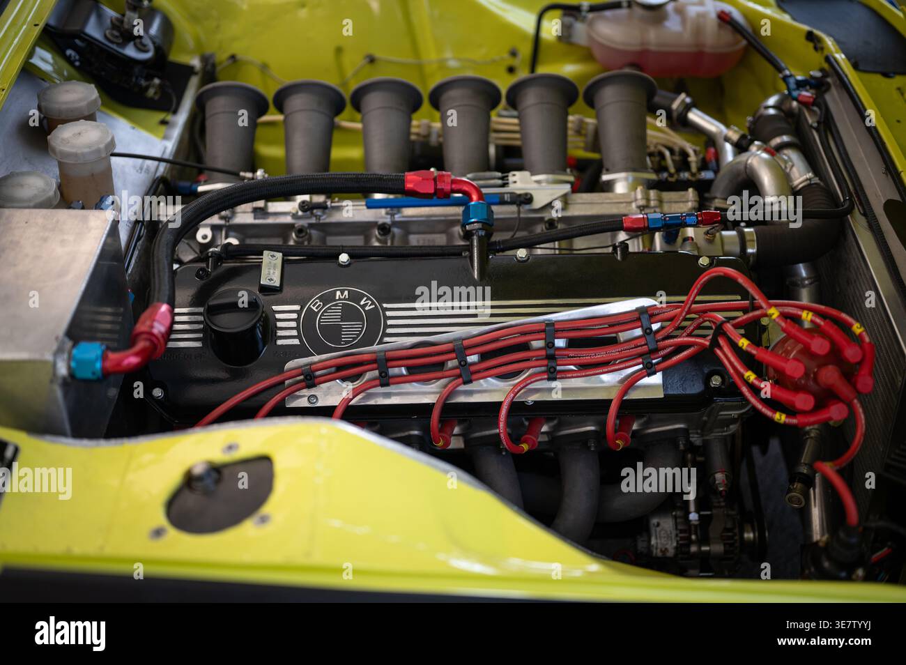 Hohe Winkeldetails eines BMW 3,0 CSL-Rennmotors mit geradem Sechszylinder-Rennmotor mit individuellen Geschwindigkeitsstapeln und roten Zündkerzendrähten in einem gelben Motor Stockfoto